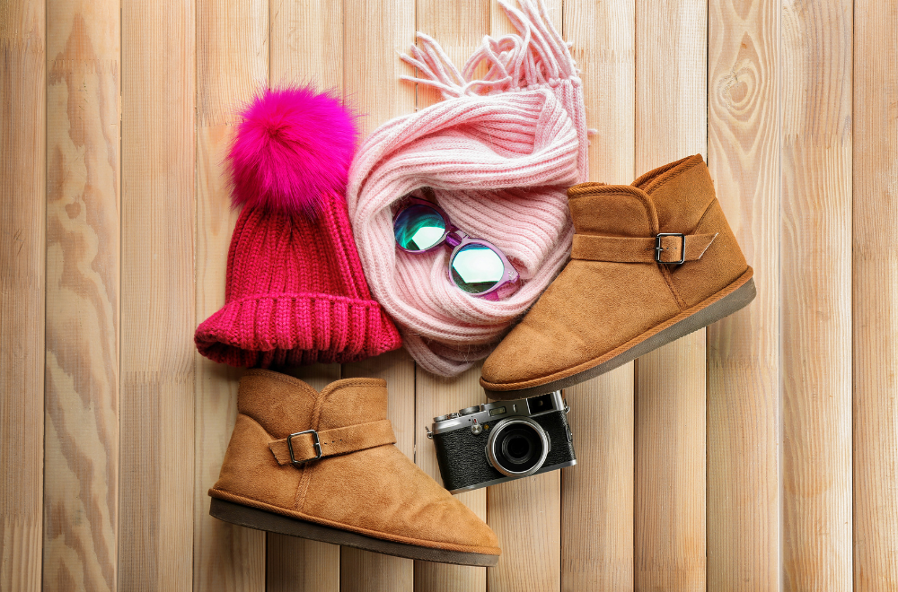 A pink hat and scarf woolen boots, glasses and a camera displayed on a table